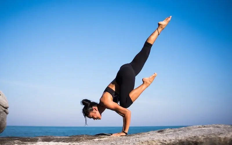 balance lady doing a yoga stretch on a rock by the water